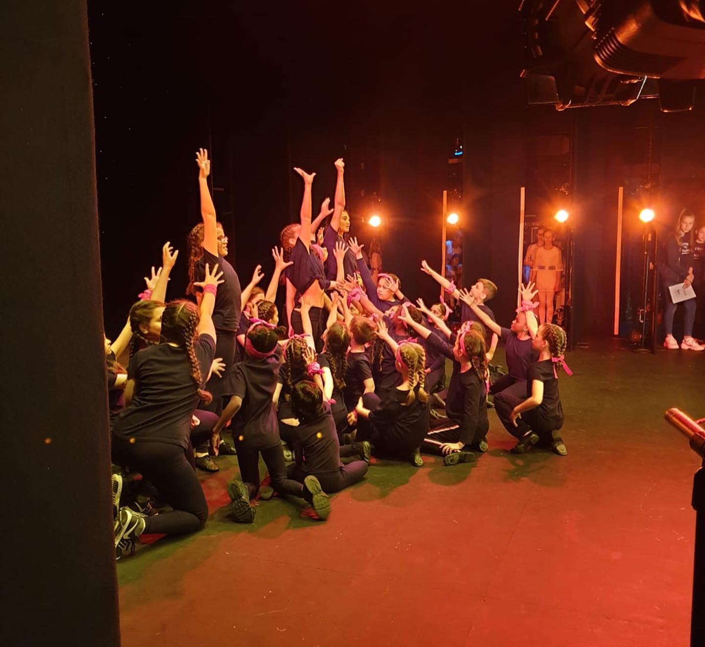 Shot from backstage looking onstage of Chrystel Arts students at the end of a dance number in a group with their arms shot in the air